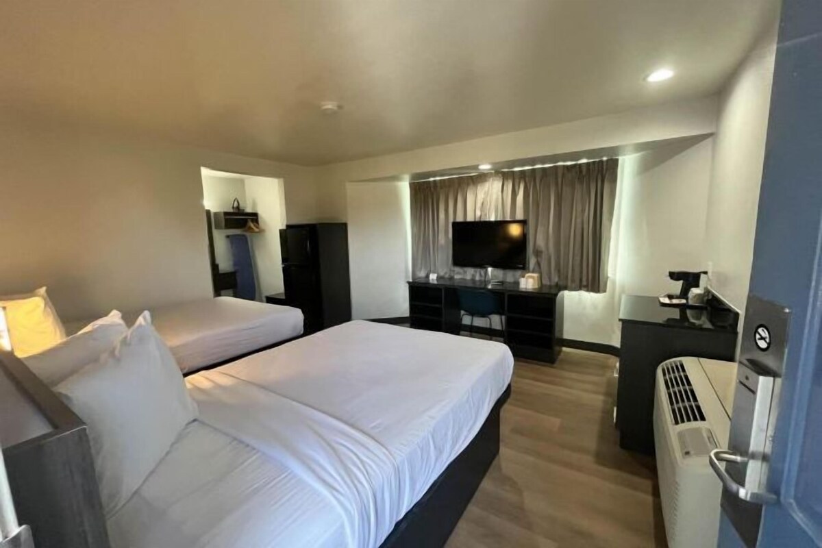 A hotel room with two beds, a TV, a desk, and a heater.