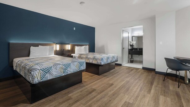 A hotel room with two beds, a desk, and a bathroom visible through an open door. - Studio 6 Suites Escondido, CA (Escondido)