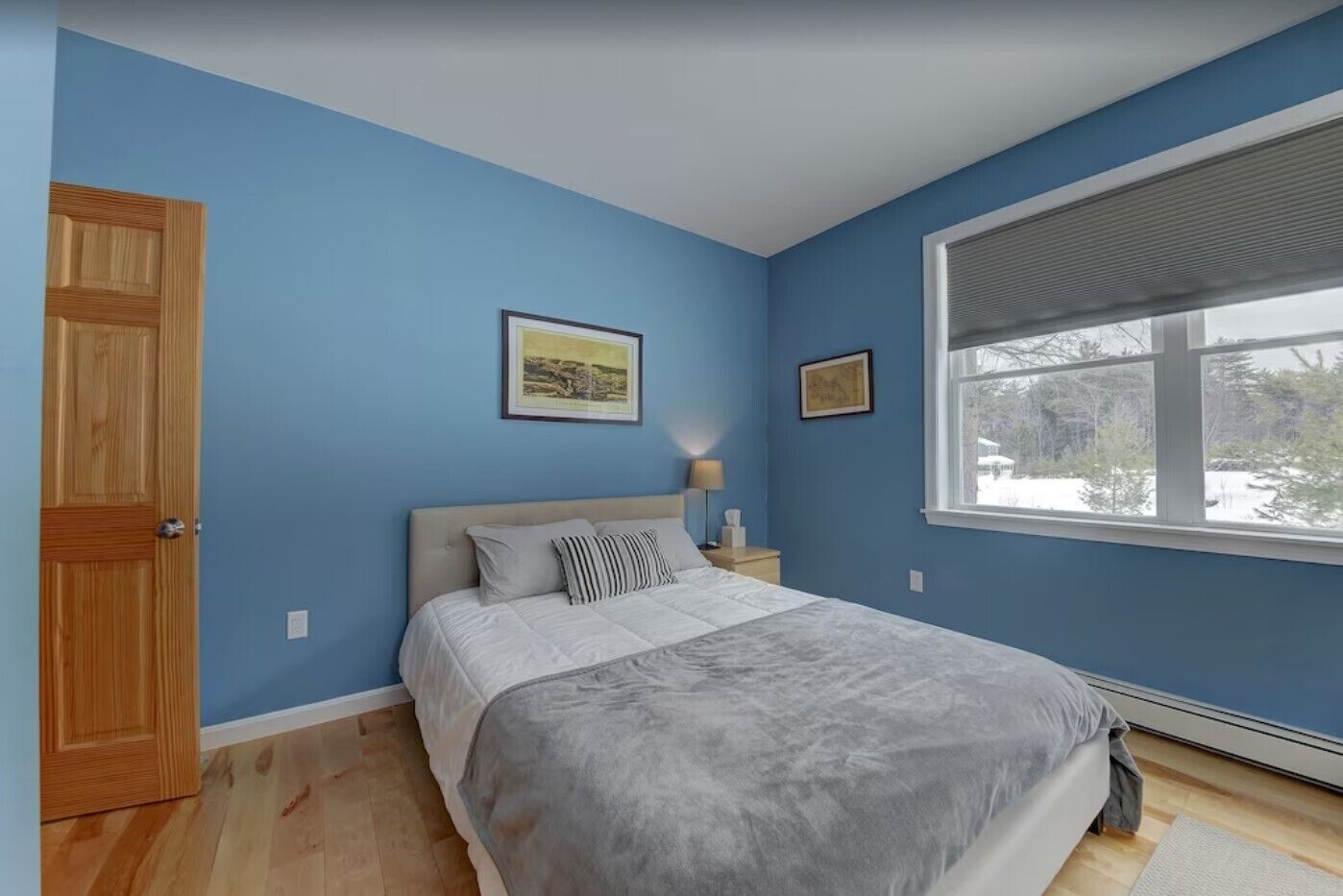 Una camera da letto con un letto, un comodino, una finestra vista alberi e una porta.