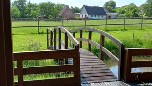 Een houten brug die leidt naar een grasveld, met een huis op de achtergrond.