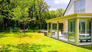 Una casa moderna con una veranda vetrata, un'amaca e mobili da esterno.