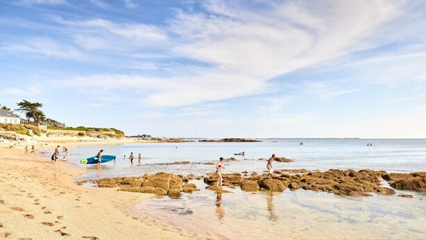 Una spiaggia con acque cristalline, zone rocciose e persone che svolgono diverse attività.