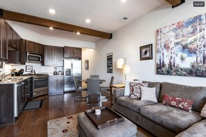 A modern kitchen with dark wood cabinets, stainless steel appliances, and a dining area with a gray sofa and a large painting on the wall.