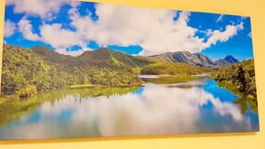 Pintura de un paisaje montañoso con un lago, árboles y cielo despejado.
