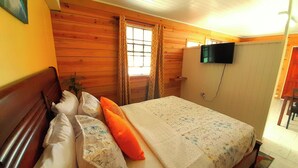 Un dormitorio con cabecera de madera, cama con ropa de cama estampada, televisor montado en la pared y ventana con cortinas.