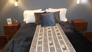 Una cama con una colcha estampada, dos almohadas blancas y una almohada gris. Hay dos mesitas de noche con pequeños objetos decorativos.