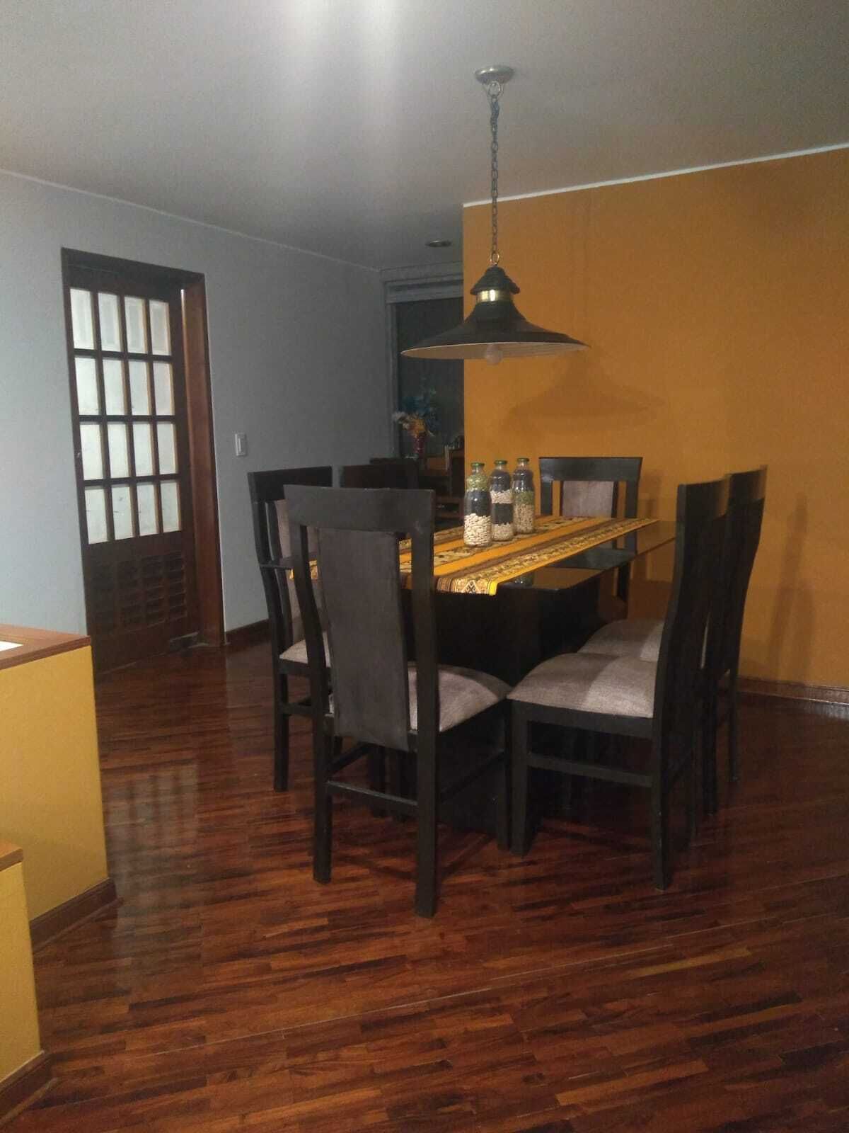 A dining area with a wooden table, four chairs, and a hanging pendant light.