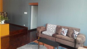 Sala de estar con un sofá marrón, un plaid estampado y almohadas, una mesa de centro negra y una mesita auxiliar de madera con una planta.