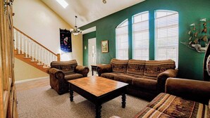 Ein Wohnzimmer mit Treppe, einer Sofagarnitur, einem Couchtisch und einer Chandelüster.