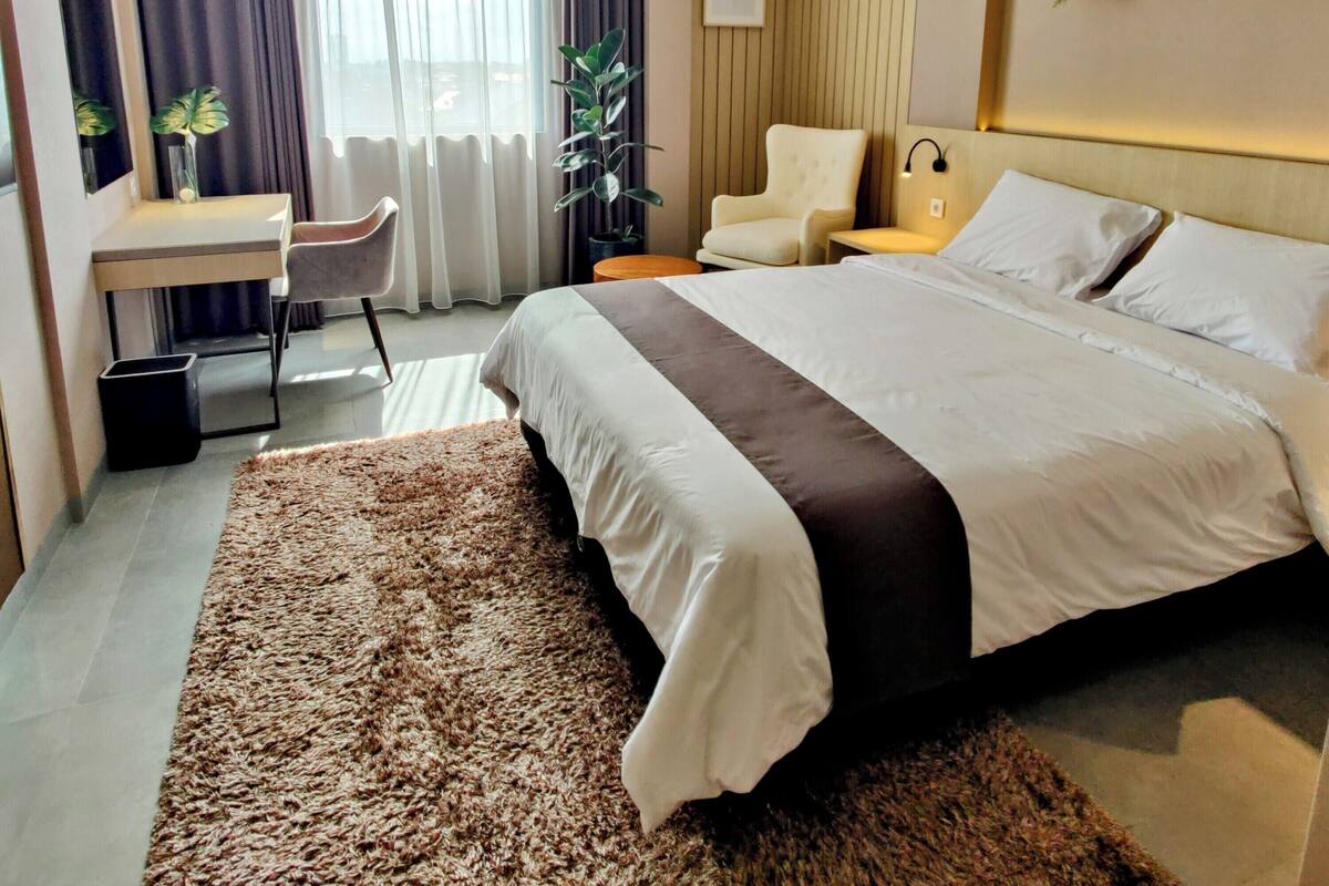 A modern hotel room with a large bed, a desk, a chair, and a small table.