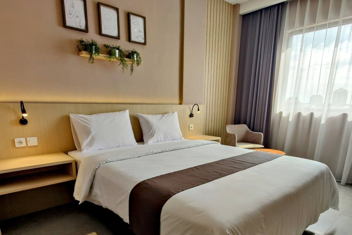 A neatly made bed with white and brown bedding, a bedside table with a lamp, and a wall-mounted shelf with plants.