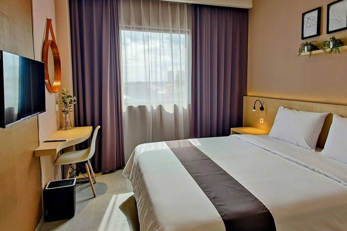 A hotel room with a bed, desk, chair, and a TV.