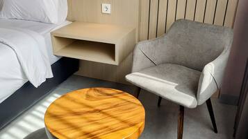 A modern hotel room with a bed, a grey armchair, and a wooden side table.