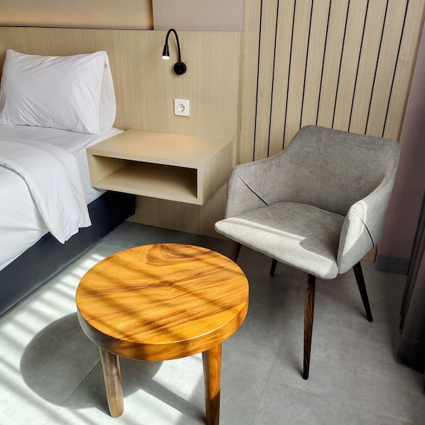 A modern hotel room with a bed, a grey armchair, and a wooden side table. - The Mango Suites by Flat06 (Jakarta)