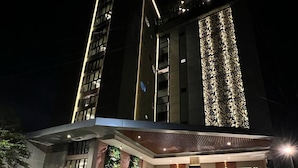 Un hôtel moderne doté d’une bande lumineuse verticale bien visible sur la façade, d’un espace d’entrée abrité agrémenté de plantes et d’un éclairage extérieur soigné la nuit.