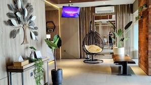 Un hall d’entrée moderne avec un plafond en bois, un grand téléviseur fixé au mur diffusant l’image « SUMMER CHILL », un fauteuil suspendu et des plantes en pot.