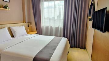 A hotel room with a large bed, a bedside table with a lamp, a TV mounted on the wall, and a window with curtains.