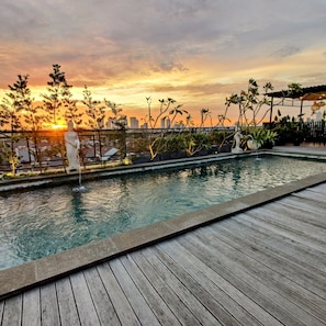 A rooftop pool with a wooden deck, surrounded by potted plants and a statue. - The Mango Suites by Flat06 (Jakarta)