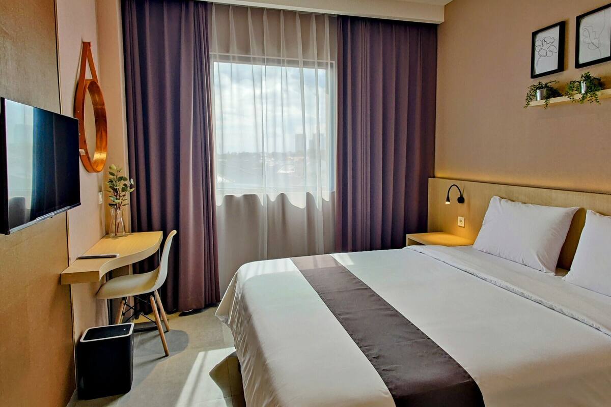 A hotel room with a large bed, a desk with a chair, a TV, and a window with curtains.