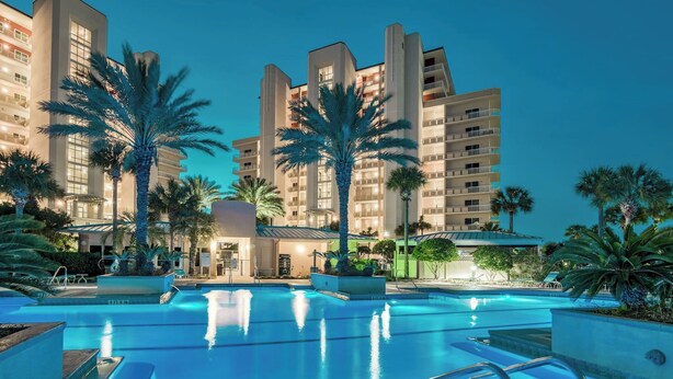 A hotel with a swimming pool, palm trees, and a modern building facade.