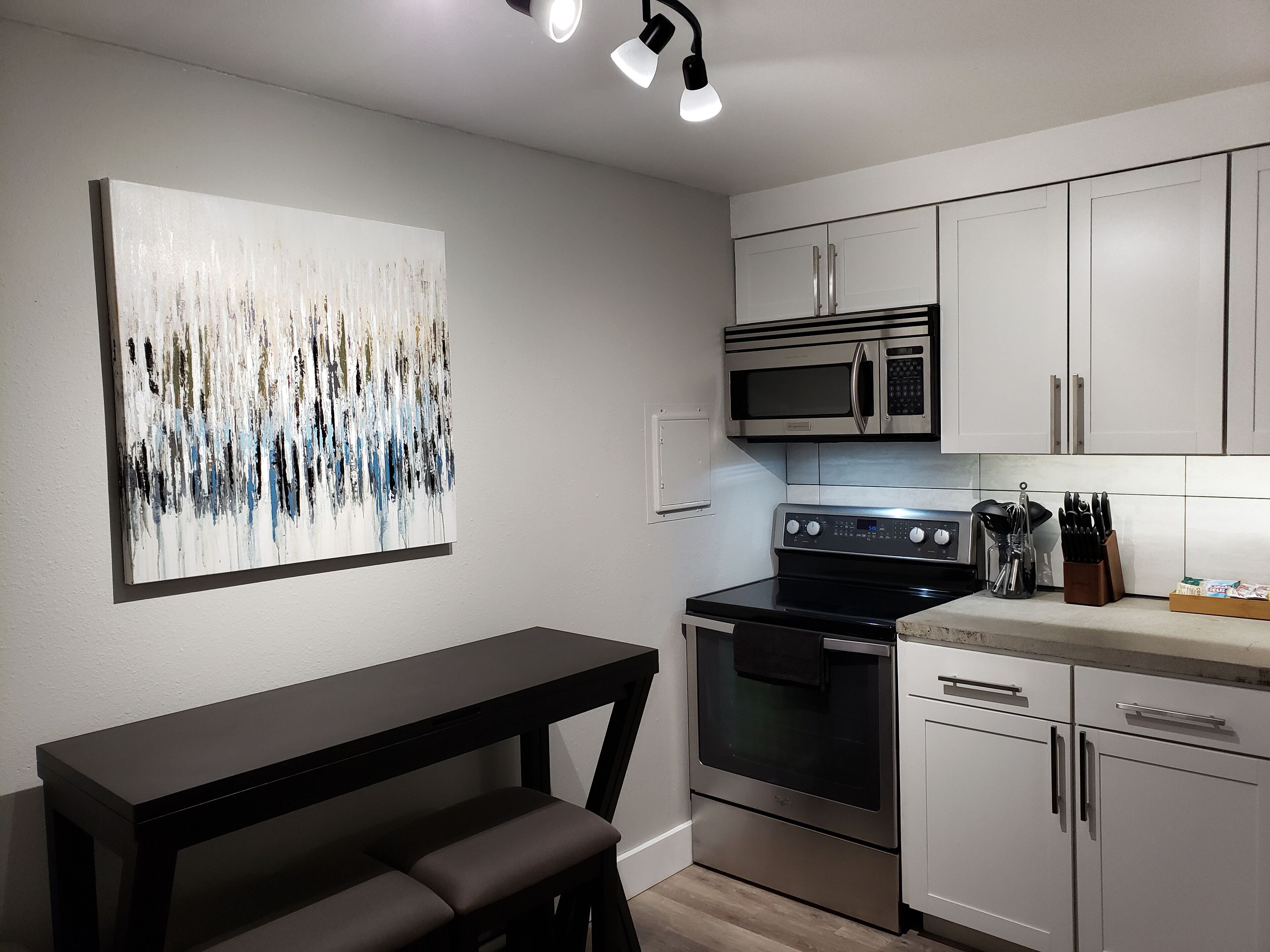 Une cuisine moderne avec des meubles blancs, une cuisinière en acier inoxydable, un four à micro-ondes et une table à manger noire avec des bancs.