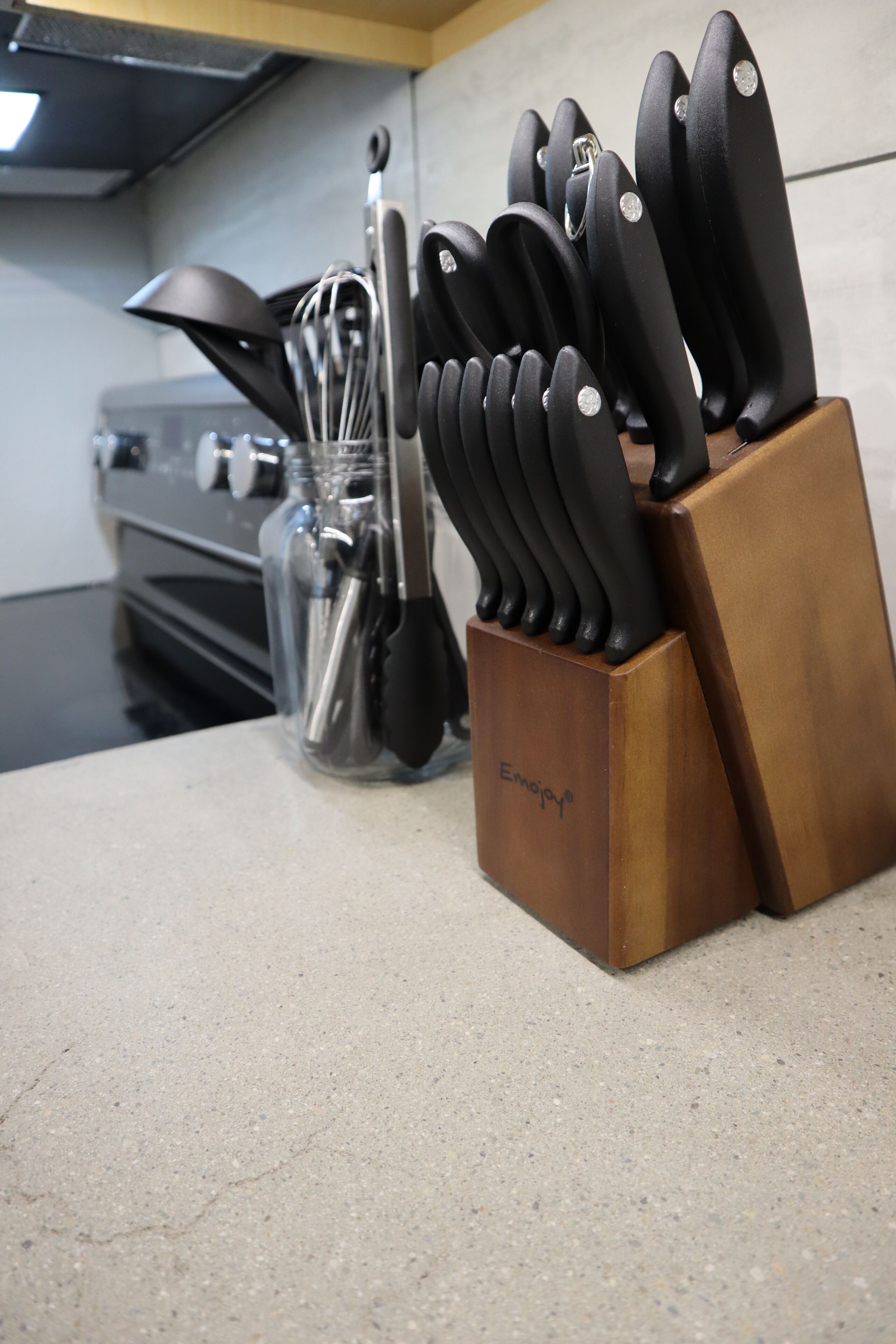Una encimera de cocina con un bloque de cuchillos y un tarro de vidrio con utensilios.