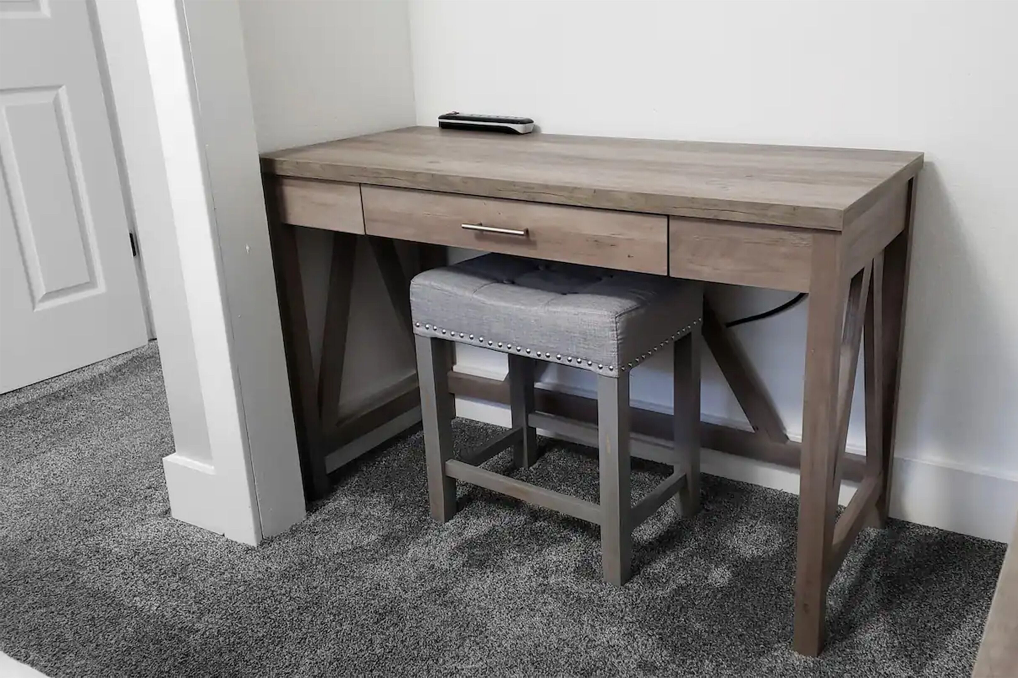 A corner desk with a drawer, a stool, and a remote control on top.