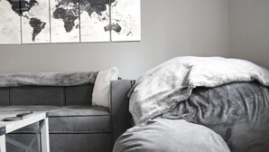 Ett minimalistiskt vardagsrum med en grå soffa, ett litet träbord och en världskarta på väggen.