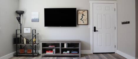 Una sala de estar con televisor de pantalla plana, una estantería, una puerta y una revista en el suelo.