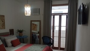 Ein Hotelzimmer mit einem großen Bett, einem kleinen Tisch mit Pflanze, einem Sessel und einer Glastür zum Balkon.