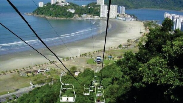 Eine Seilbahn über einem Strand mit Blick auf den Ozean und Gebäude im Hintergrund.