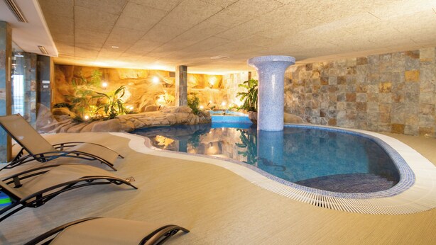 Una piscina interna con lettini, un muro in pietra e una fontana decorativa.