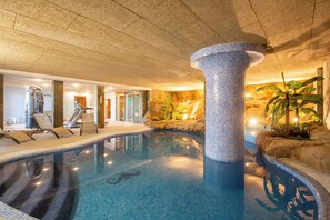 An indoor swimming pool with a tiled column, lounge chairs, and a tropical wall design.