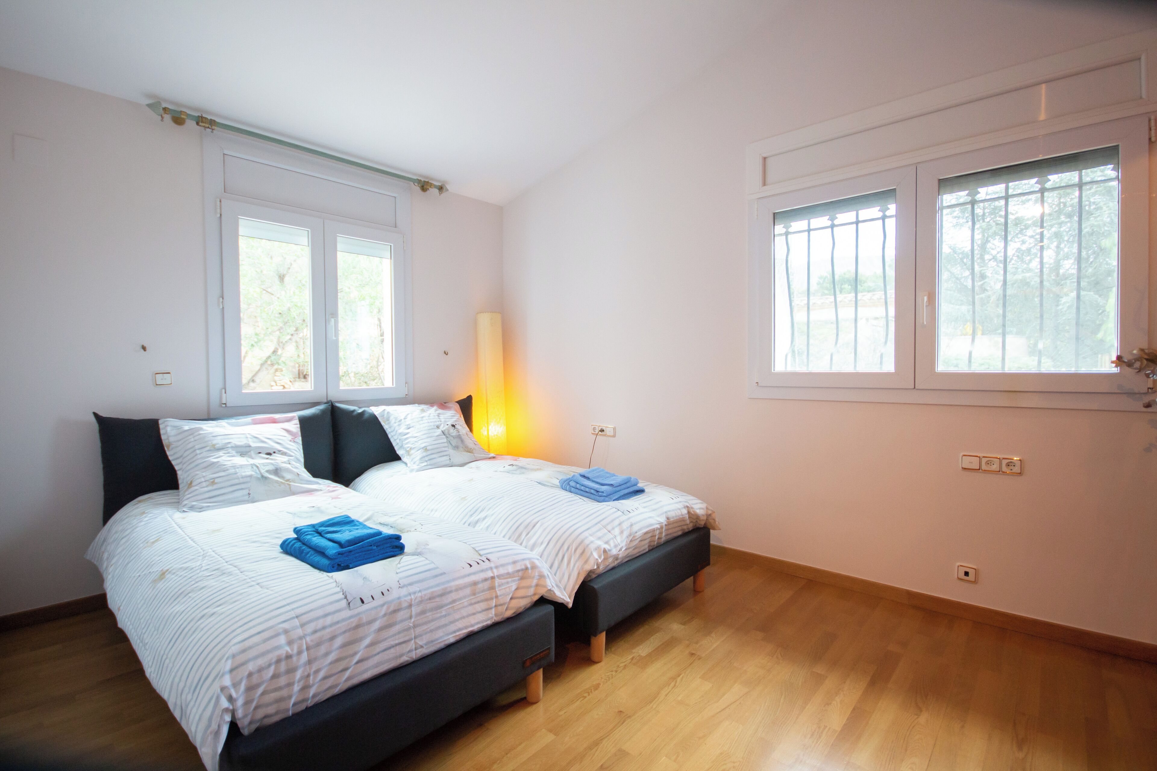 Une chambre avec deux lits, une lampe de chevet et une fenêtre donnant sur des arbres.