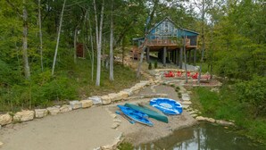 Un chalet au bord du lac, doté d’un quai, entouré d’arbres et accessible par un sentier de pierres qui mène à l’eau.