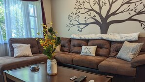 Un salon avec un canapé en cuir marron, une table basse et une fresque murale représentant un arbre.