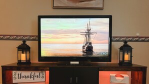 Un téléviseur posé sur un meuble en bois, avec deux lanternes allumées, une pancarte sur laquelle est écrit « merci » et le logo « Cook Airbnb ».