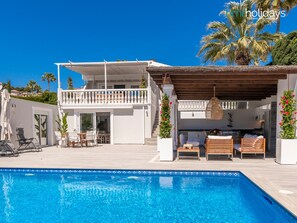 Uma área de piscina com piscina, mobiliário de exterior e um alpendre coberto.