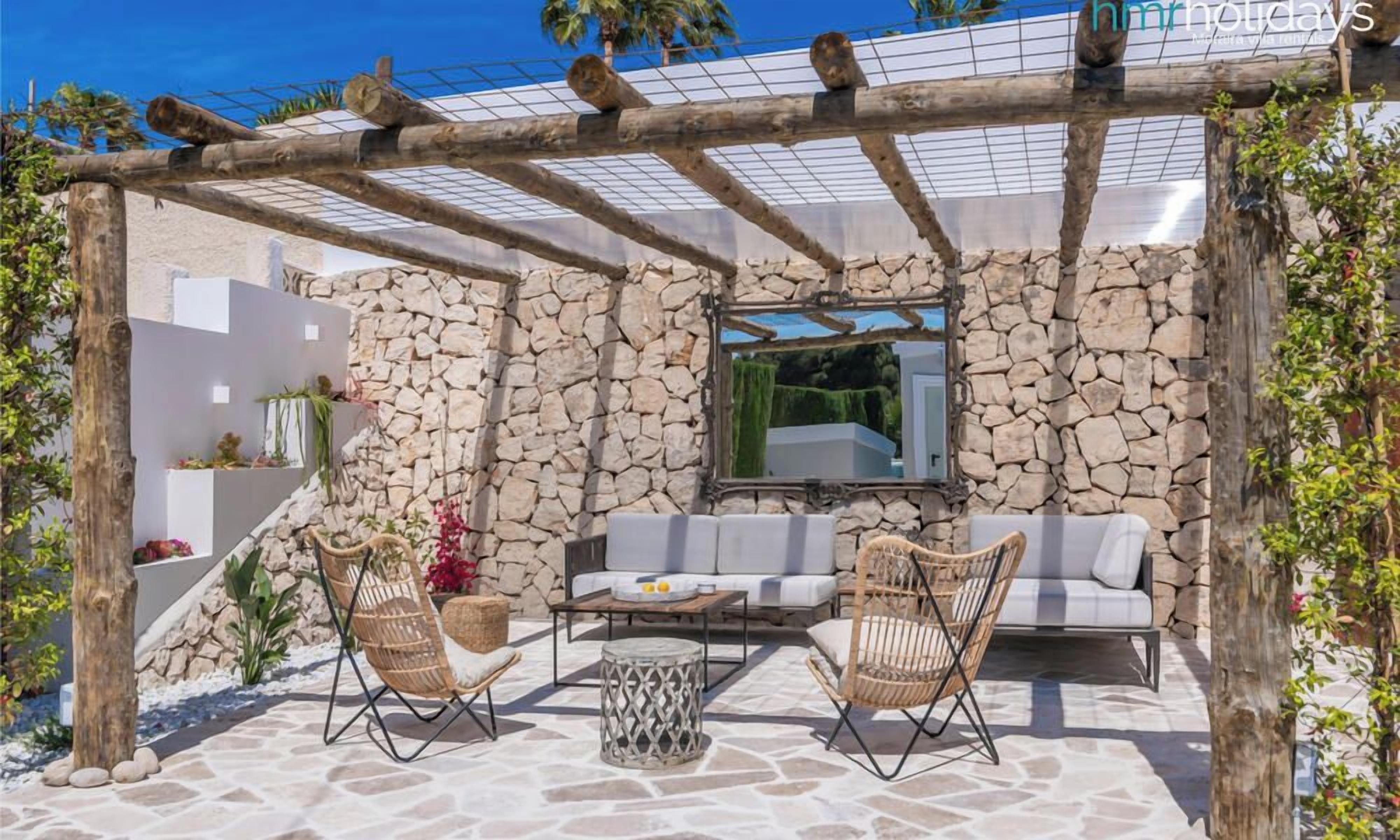 An outdoor patio with stone flooring, a wooden pergola, a sofa, two wicker chairs, and a coffee table.