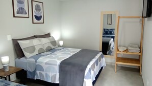 Un dormitorio ordenado con cama, lámparas de noche, un espejo y una repisa de madera con ropa doblada.