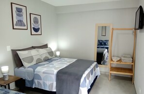 Relax in a serene bedroom with a neatly made bed, abstract artworks, and a convenient shelf for essentials.