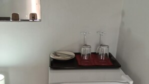 Un refrigerador blanco pequeño con un estante superior negro, un mantel individual rojo y dos copas de vino encima.