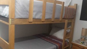 Un letto a castello con struttura in legno, biancheria grigia e un comodino con una lampada.