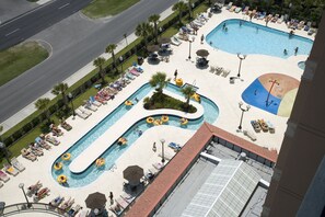 Relax by the rooftop pool, surrounded by lounge chairs and umbrellas, with a winding water feature and multiple seating areas.