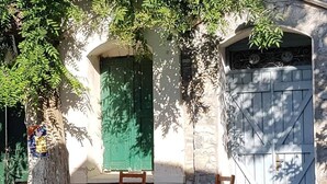 A building with a stone facade, a green door, and a blue gate. There are two wooden chairs and a small table outside. - Aegean tradiotional cottage in Akamatra Ikaria (akamatra ikaria)