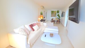 Un salon moderne avec un canapé blanc, une table basse et, au fond, un coin repas.
