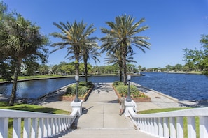 A pathway leading to a body of water with palm trees and a white fence.