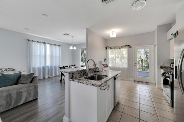 A modern kitchen with a central island, a dining area with a bench, and a living room with a sofa.