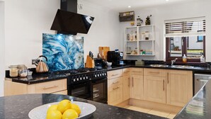 A modern kitchen with a large island, black stove, wooden cabinets, and a marble backsplash. - Woodfield House - Beautiful Tenby Cottage (Tenby)