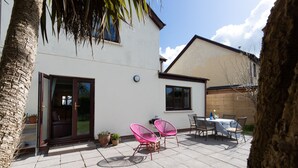 A patio with a table and chairs, a sliding glass door, and potted plants. - Woodfield House - Beautiful Tenby Cottage (Tenby)